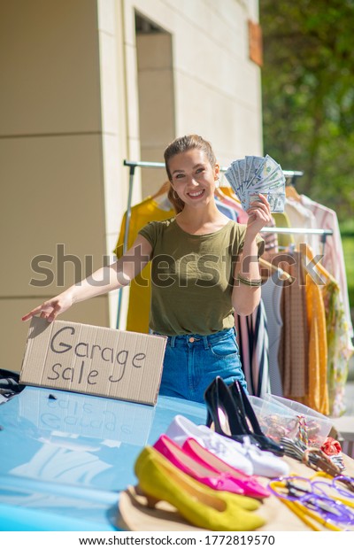 Successful garage sale. Pretty\
happy woman holding her daily income while having a successful\
sale