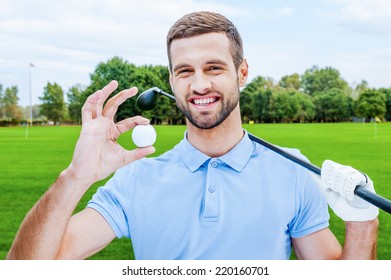 Successful Golfer. Happy Young Man Holding Golf Ball And Driver While Standing On Green