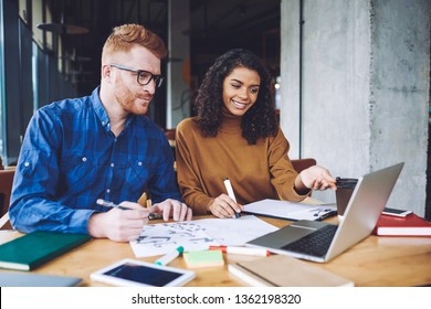 Successful Graphic Designers Creating New Logo For Company During Collaboration In Coworking Space, Positive Multicultural Male And Female Hipsters Enjoying Time For Cooperation On Laptop Device