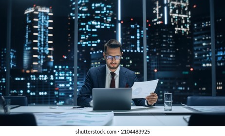 Successful Handsome Businessman Working on Laptop Computer in Big City Office Late in the Evening. Finance Investment Analyst Checking Line and Pie Graphs from Project Management Report.