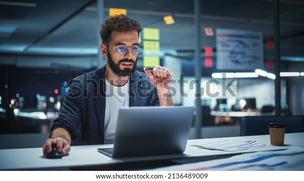 Successful Handsome Creative
Director Working on Laptop Computer in Big City Office Late in the
Evening. Businessman Preparing for a Marketing Plan in Conference
Room.