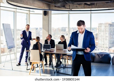 Successful Handsome Male Mentor, Director, Businessman In A Suit At The Office. Working Day Concept. Team Meeting With The Boss In The Foreground