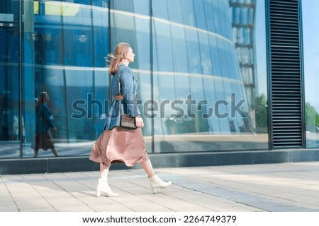 Successful happy woman on her way to work in street. Confident business woman with a smile in stylish clothes. Smiling lady steps on the background of the business center walk along the city street.