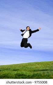successful and happy young adult businessman running and jumping in the green field