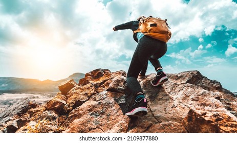 Successful hiker with backpack climbing the mountain on sunset - Traveler woman standing on the top of the rock pointing the landscape - Freedom, success and extreme sport concept