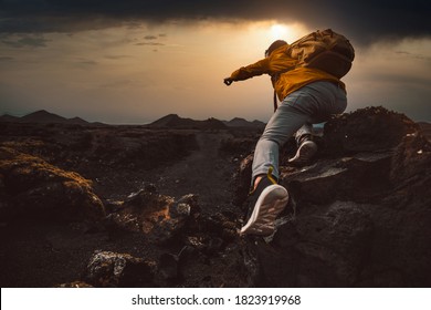 Successful hiker hiking a mountain pointing to the sunset. Wild man with backpack climbing a rock over the storm. Success, wanderlust and sport concept.