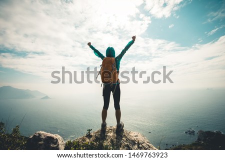 Successful hiker outstretched arms at seaside mountain top cliff edge