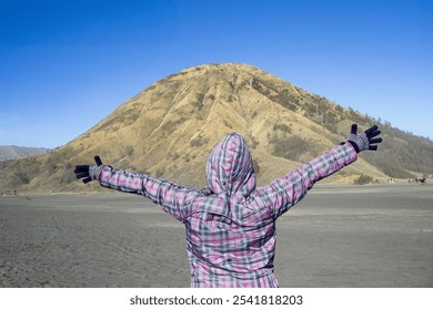 A successful hiker woman with a jacket standing in the desert in front of a mountain with hands up and the blue sky, achieving the best result of self motivation. - Powered by Shutterstock