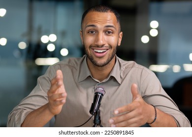 Successful hispanic man inside office looking at camera and talking on video twin inside office, businessman recording audio podcast using professional microphone, webcam view pov. - Powered by Shutterstock