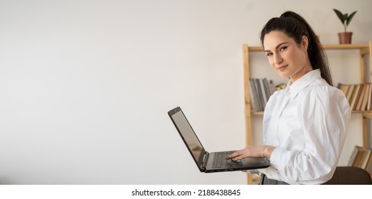 Successful Hispanic Millennial Woman Using And Typing On Laptop In Modern Office Looking At Camera. Female In Business Concept. Banner