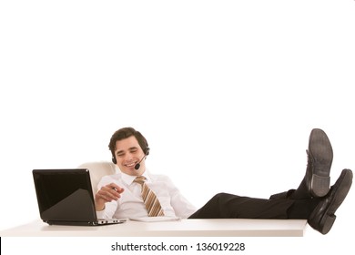 Successful or lazy businessman relaxing at his desk with his feet up on the desktop while talking on a headset