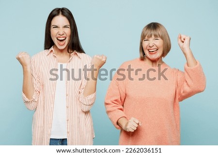 Successful lucky happy fun elder parent mom with young adult daughter two women together wear casual clothes do winner gesture clench fist isolated on plain blue cyan background. Family day concept