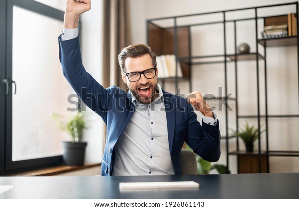 Successful lucky young bearded businessman in\
formal wear raised fists up celebrating success, screaming yes,\
passed test with high score, got promoted, won lottery, closed a\
deal. Victory\
concept