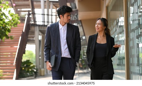 Successful male boss and female executive manager chatting while walking along apart of the office building. Urban office life with Asian businesspeople.