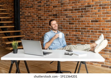 Successful male entrepreneur takes a break on the workplace, hipster guy sits in relaxed pose with his feet on the table and resting with a cup of coffee in the modern office space - Powered by Shutterstock