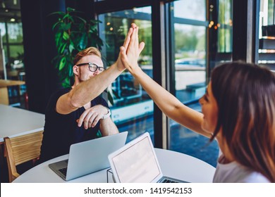 Successful Male And Female Freelancers High Five To Each Other And Feeling Good From Well Done Work With It Project, Partners Enjoying Cooperation Sitting At Table With Netbook With Mock Up Screen