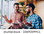 Successful male startuppers discussing plan together for work smiling and gesturing, happy hipster guys having friendly conversation about business information having meeting in coworking office