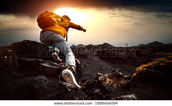 Successful man hiking mountains at sunset\
- Hiker with backpack pointing the sky with\
finger
