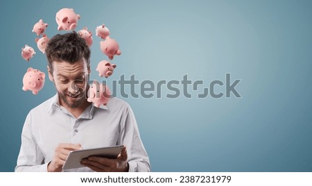 Successful man investing money online, he is using a digital tablet and he is surrounded by many piggy banks