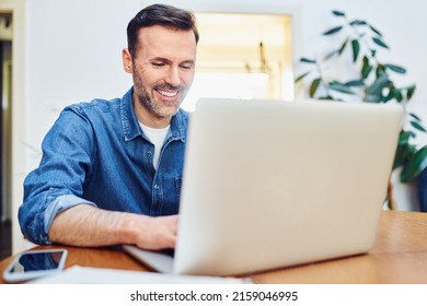 Successful Man Working On Laptop Sitting At Table At Home