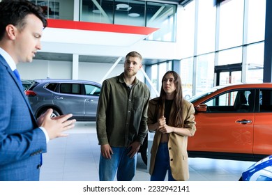 A successful manager shows a young couple new cars that are available at the dealership - Shutterstock ID 2232942141