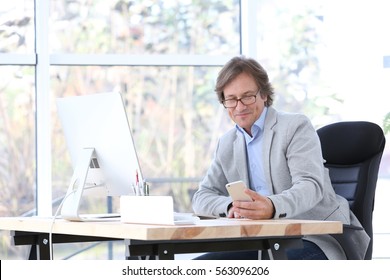 Successful Mature Man With Mobile Phone In Office