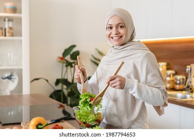 Successful mature middle-eastern wife woman in hijab cooking vegetable salad, preparing vegan vegetarian food at home in the kitchen. - Powered by Shutterstock