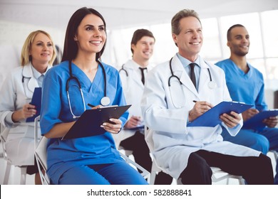 Successful medical doctors are making notes and smiling while sitting at the conference