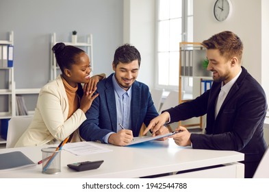 Successful Meeting With Broker Bank Agent Insurer. Happy Mixed Ethnicity Couple Customers Sign Mortgage Loan Contract. Smiling African American Wife Hugs Caucasian Husband Putting Signature On Paper