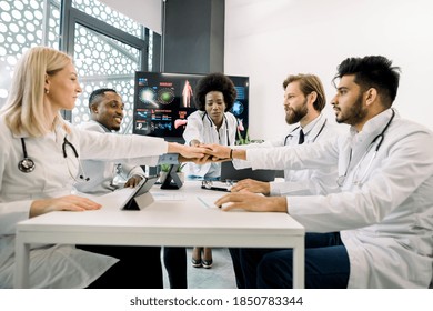 Successful meeting, teamwork concept. Multiracial healthcare experts, doctors, coordinating, stacking their hands together, while having a meeting at modern clinic