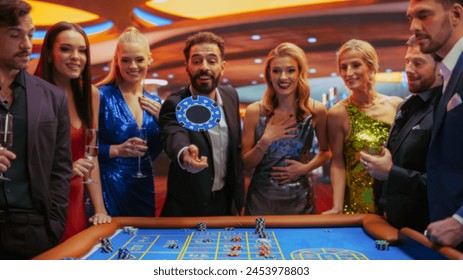 Successful Men and Women Partying in Luxurious Casino. Young People Gambling at a Roulette Table, Putting High Stakes Bets. Man Tossing a Blue Chip with a Placeholder, Crowd Cheering, Enjoying Drinks