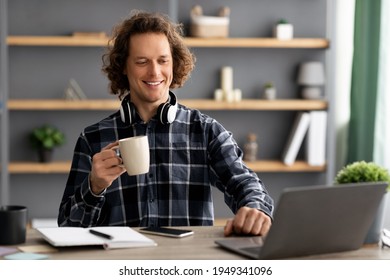 Successful Millennial Businessman At Laptop Drinking Coffee Enjoying Work Sitting At Workplace. Young Empolyee Worker Using Computer In Modern Office. Business People And Entrepreneurship