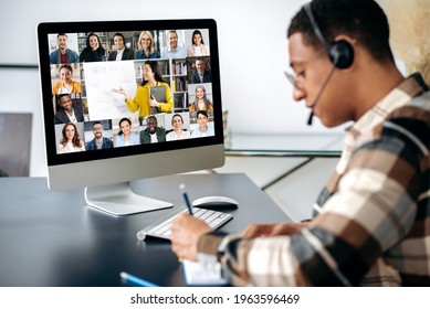 Successful Mixed Race Clever Male Student Learning Distantly. At Laptop Screen Female Teacher And Students. Teacher Conducts Online Lecture, Male Student With Headset Takes Notes. Video Call