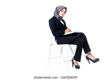 Successful Muslim Businesswoman Sitting Down. Holding Book And Pen. Isolated White Background.