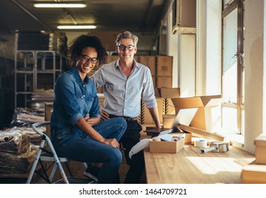 Successful online shop business partners in a small office. Male and female entrepreneurs at their online shop warehouse looking at camera and smiling.