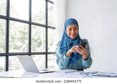 Successful Pretty Asian Muslim Lady In Hijab Make A Phone Call When Working At Desk In Office During Working On Her Project On Laptop Computer.