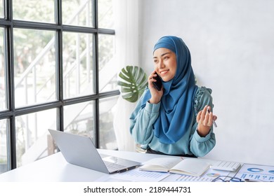 Successful Pretty Asian Muslim Lady In Hijab Make A Phone Call When Working At Desk In Office During Working On Her Project On Laptop Computer.