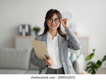 Successful psychologist. Portrait of arab female psychologist holding clipboard, smiling at camera in modern office. Confident psychoanalyst posing at mental health clinic - Shutterstock ID 2090152072