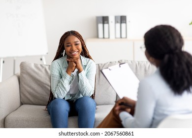 Successful psychotherapy. Millennial female client having session with psychologist, smiling, sitting on couch at clinic. Cheerful black lady communicating with therapist, solving emotional problem - Shutterstock ID 2067560861