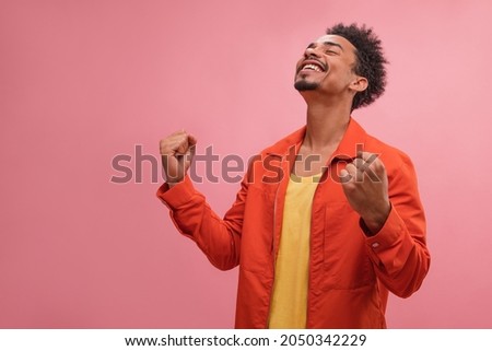 Successful reception of emotional and positive African young and happy man. Well-dressed, combed guy with curly brunette hair and toothy smile closed his eyes and took moment of joy.