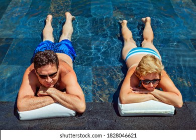 Successful Retirement Recreation, Summer Vacation Concept. Retired Mature Couple Enjoying Beautiful Sunny Day In Swimming Pool At Beach Club. Happy Senior Woman And Man Lying In Water At Poolside.