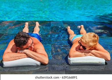 Successful Retirement Recreation, Summer Vacation Concept. Retired Mature Couple Enjoying Beautiful Sunny Day In Swimming Pool At Beach Club. Happy Senior Woman And Man Lying In Water At Poolside.