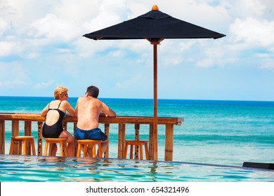 Successful Retirement Recreation, Summer Vacation Concept. Retired Mature Couple Enjoying Beautiful Sunny Day In Swimming Pool At Beach Club. Happy Senior Woman And Man Sitting At Poolside Beach Bar.