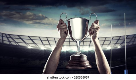 Successful rugby player holding trophy against rugby stadium - Powered by Shutterstock