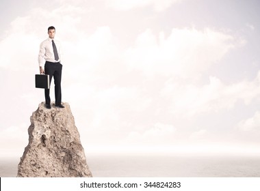 Successful Sales Person With Brief Case Standing On Top Of A Mountain Cliff Edge Looking Above The Landscape Between The Clouds