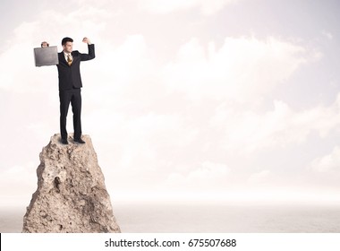 Successful Sales Person With Brief Case Standing On Top Of A Mountain Cliff Edge Looking Above The Landscape Between The Clouds