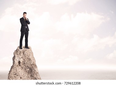 Successful Sales Person With Brief Case Standing On Top Of A Mountain Cliff Edge Looking Above The Landscape Between The Clouds