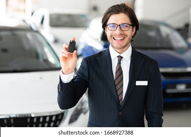 Successful Salesperson. Handsome Agent In Specs Showing Auto Key Standing In Automobile Rental Office, Free Space