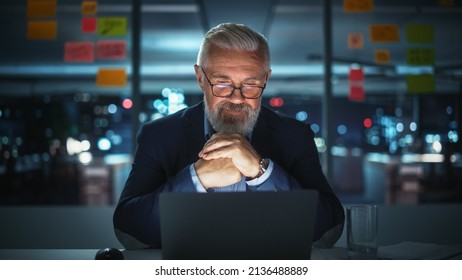 Successful Senior Businessman Working on Laptop Computer in Big City Office Late in the Evening. Investment Analyst Checking Financial Management Reports, Working with Documents - Powered by Shutterstock