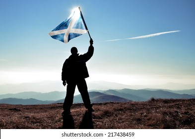 Successful Silhouette Man Winner Waving Scotland Flag On Top Of The Mountain Peak